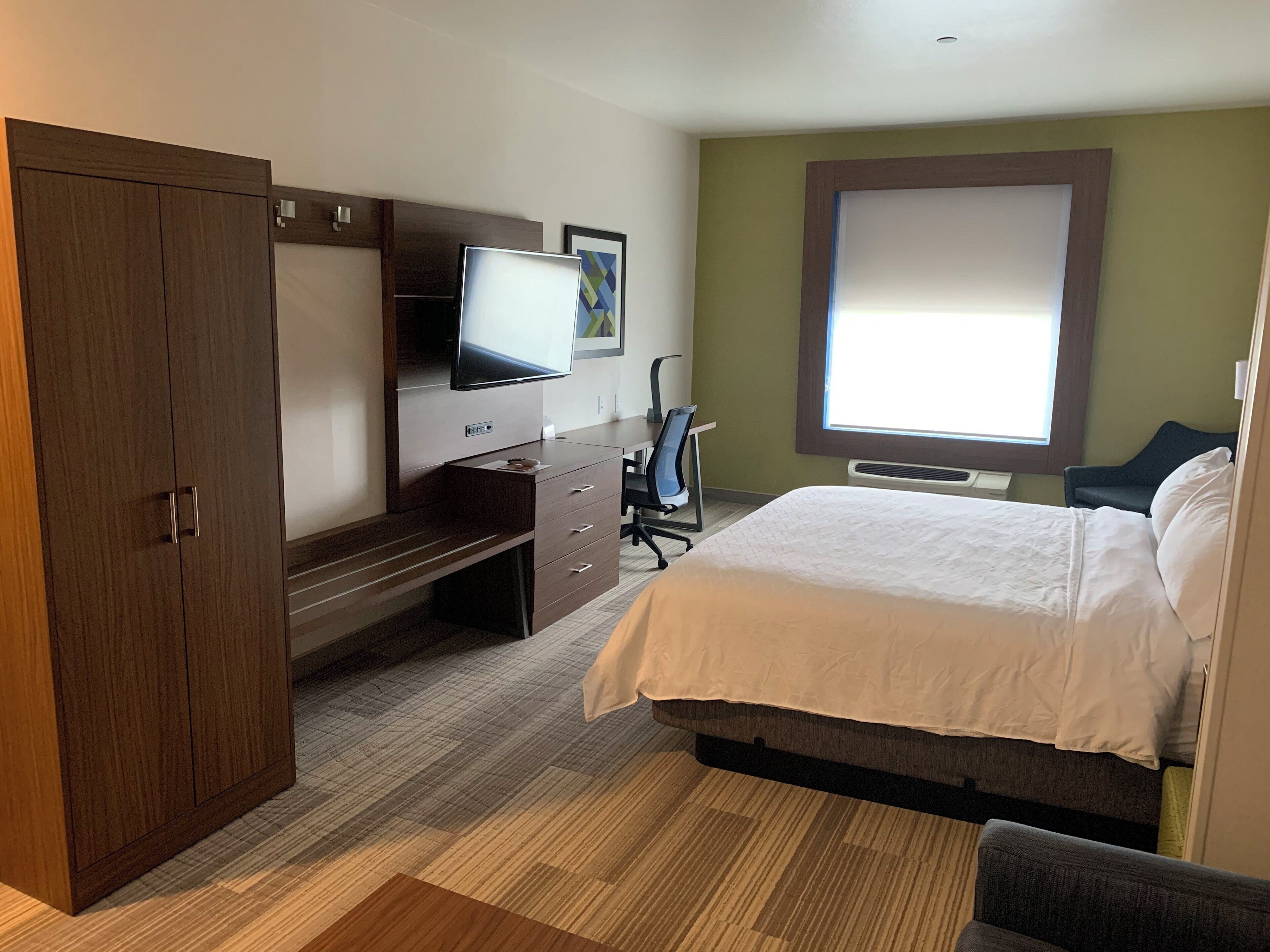 Une chambre d’hôtel comprenant un lit, un bureau avec une chaise, une télévision et une armoire.