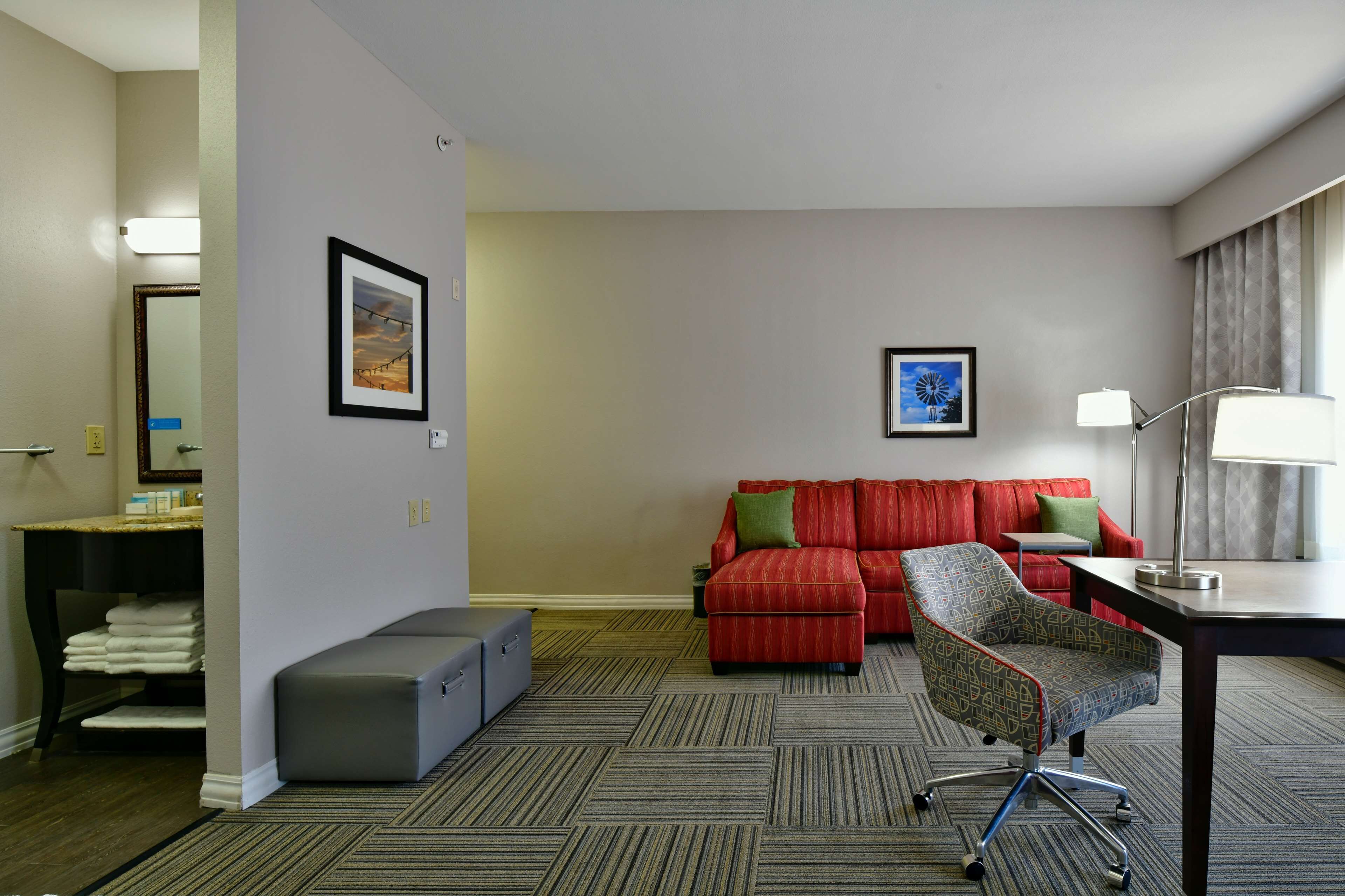 A hotel room with a bed, a desk, a chair, a sofa, and a carpeted floor.