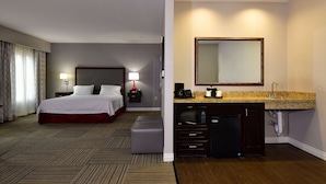 A hotel room with a bed, bedside table, lamp, and a kitchenette with a microwave and coffee maker. - Hampton Inn & Suites Fredericksburg (Fredericksburg)