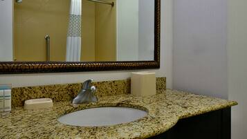 A bathroom with a granite countertop, a sink, a mirror, a towel rack, and a toilet paper dispenser.