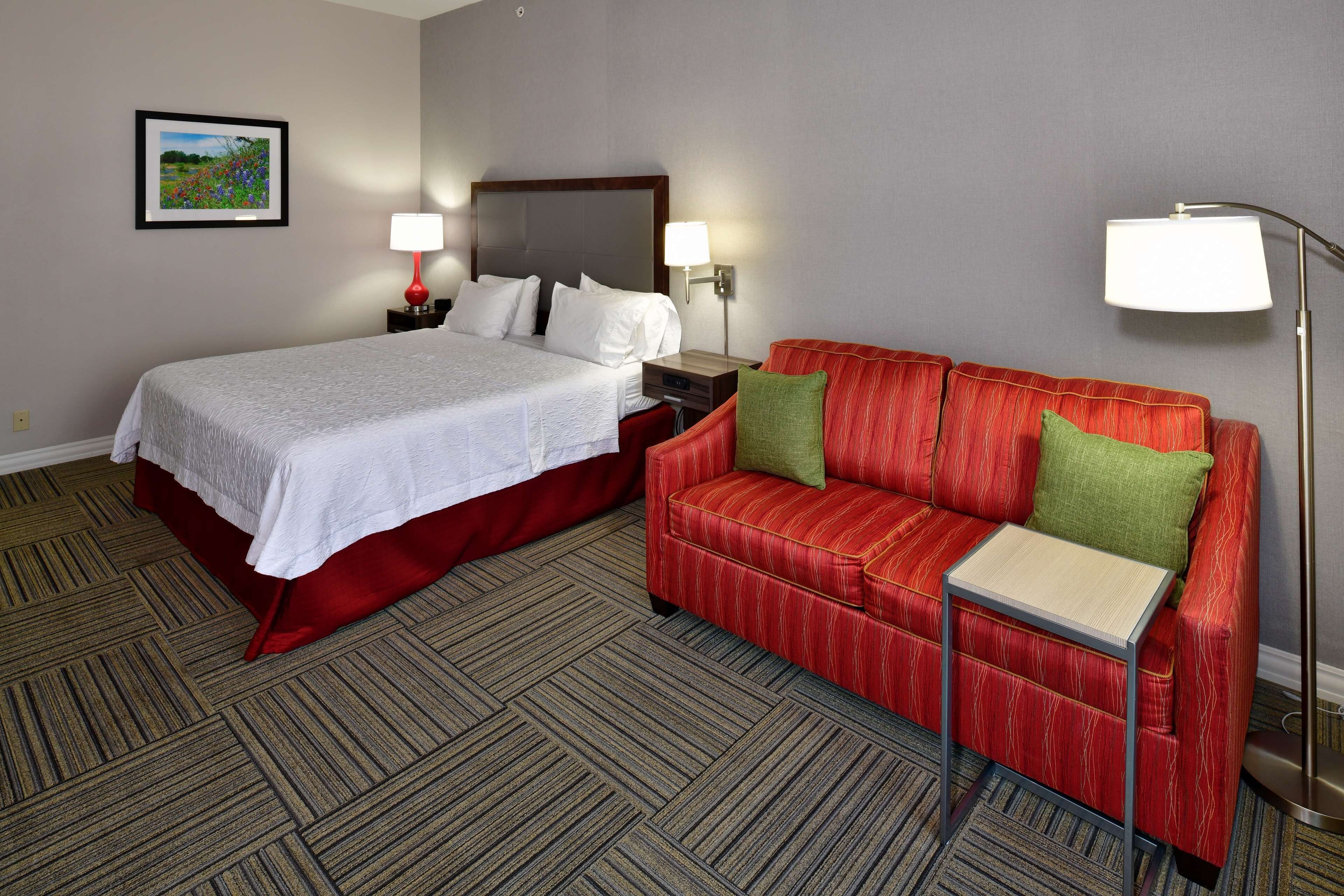 Een hotelkamer met een bed, een rode bank, een kleine tafel, een nachtkastje en twee wandlampen.