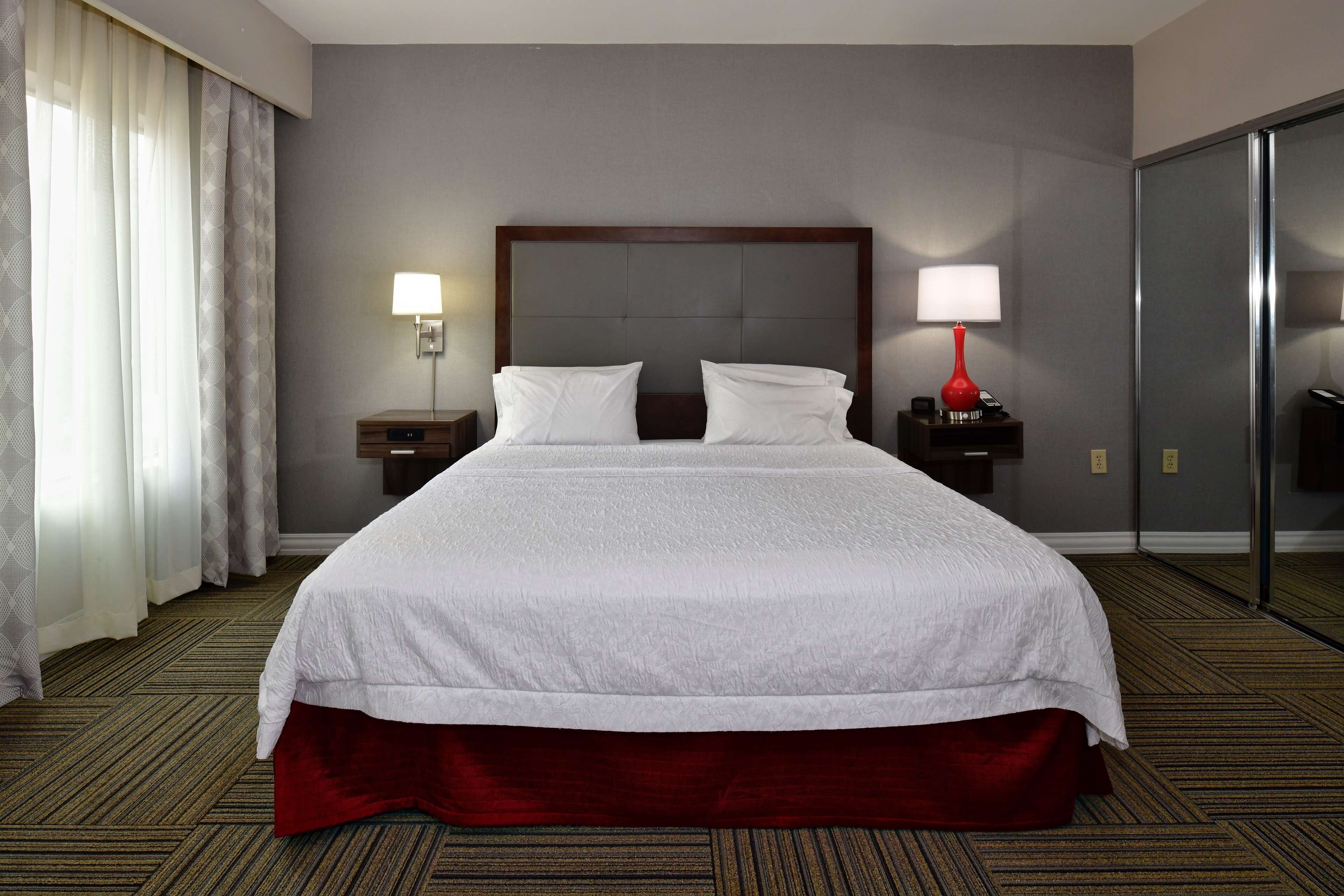 Quarto de hotel com uma cama grande, duas mesas de cabeceira com abajures, um espelho e uma porta de correr.