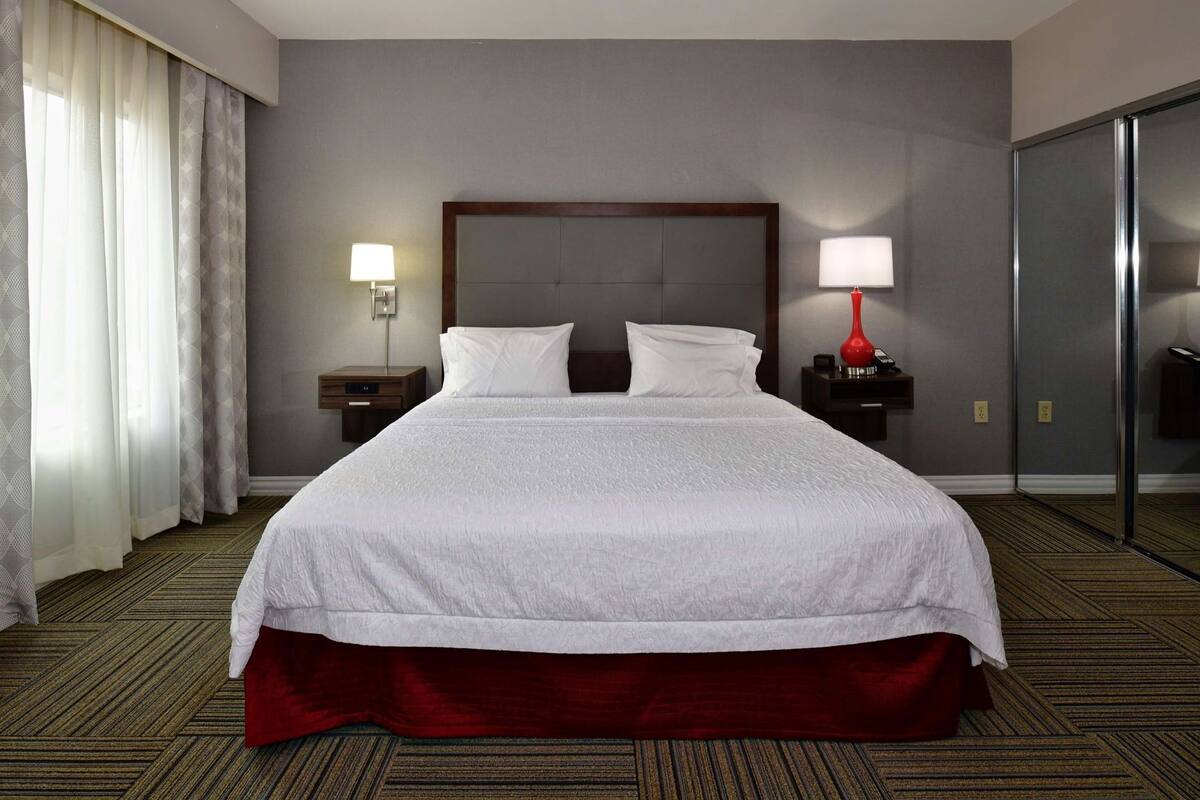 Hotelkamer met een groot bed, twee nachtkastjes met lampen, een spiegel, een kledingkast en een vloerbedekking.