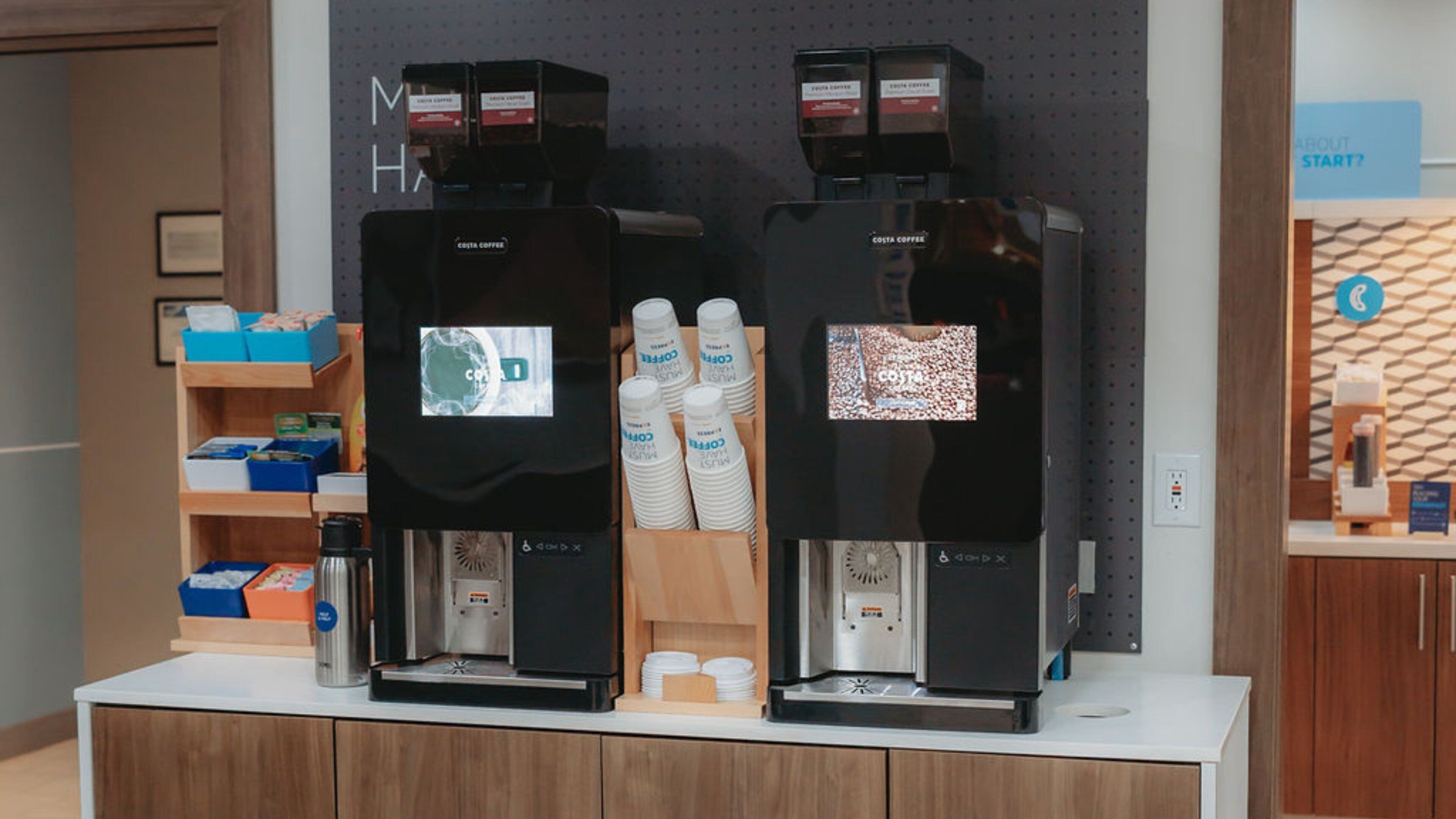 Due macchine da caffè con display digitale, un bancone in legno e una parete con un cartello.