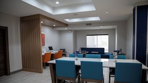 A modern dining area with a long table and blue chairs, a wooden partition, and a window with a view.