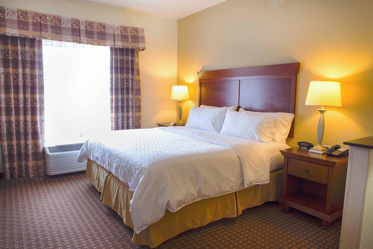 A hotel room with a bed, two bedside lamps, a nightstand with a phone, and a window with curtains.