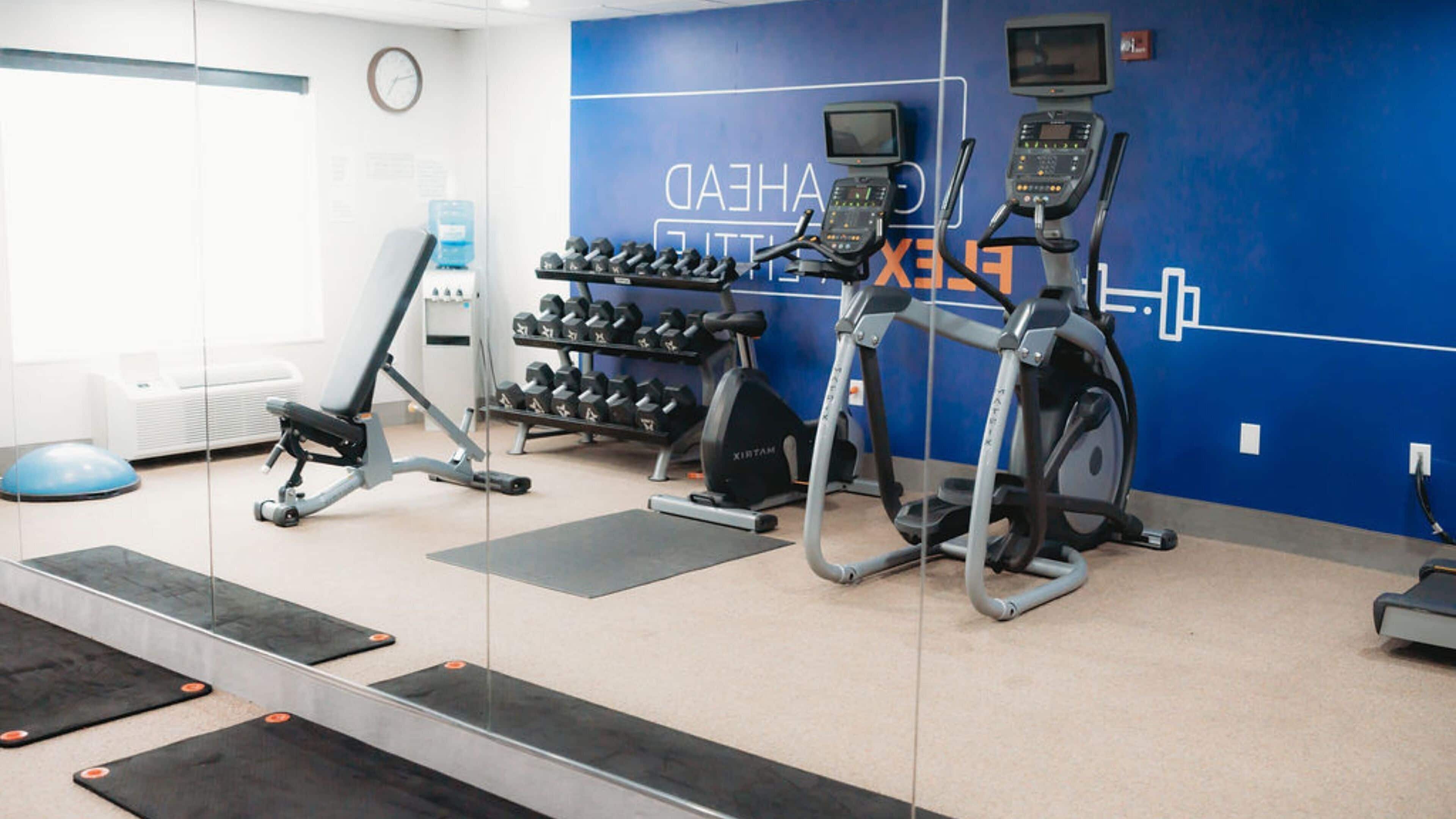 Une salle de sport équipée de matériel d’exercice, d’un distributeur d’eau et d’une horloge au mur.