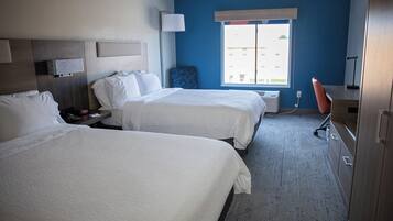 A hotel room with two beds, a desk, a chair, a lamp, and a window with a view.