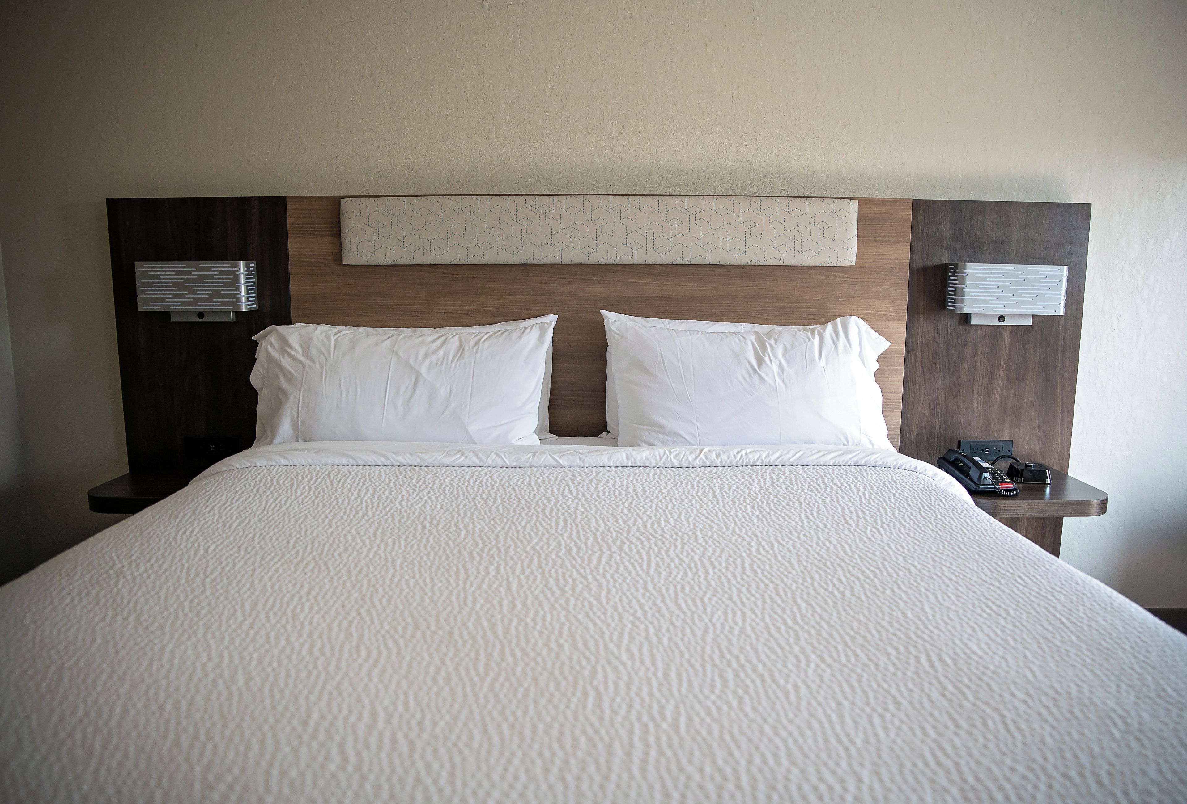 A hotel room with a large bed, two bedside tables, and a headboard with a geometric pattern.
