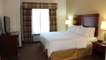 A hotel room with a large bed, a dresser, a television, and a window with curtains.