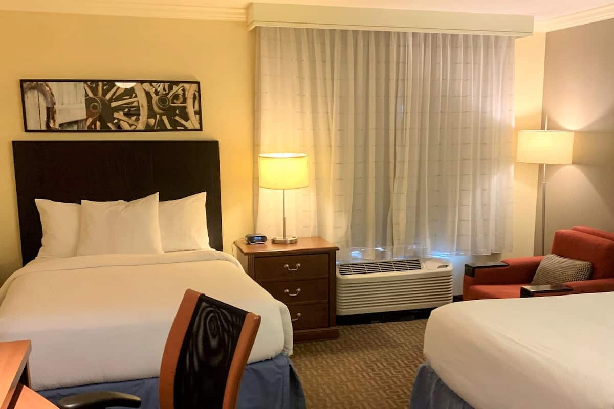 Une chambre d’hôtel avec deux lits, un bureau, une chaise, une table de chevet, une lampe et un appareil de climatisation.
