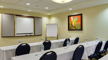 Un salón de conferencias con mesas, sillas, una pizarra y un dispensador de agua.