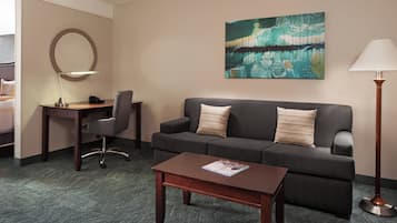 A hotel room with a sofa, a desk with a lamp, a coffee table, and a painting on the wall.