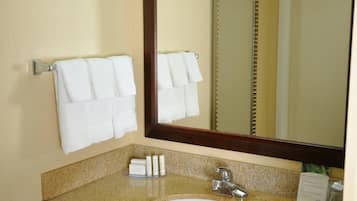 A bathroom with a granite countertop, a white sink, a mirror, and two white towels hanging on a towel rack.