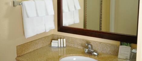 A bathroom with a granite countertop, a white sink, a mirror, and two white towels hanging on a towel rack.