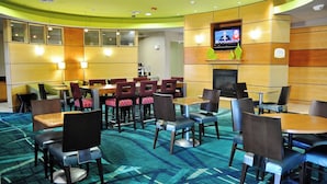 Un hall d’hôtel doté de plusieurs espaces de détente, comprenant des tables et des chaises, un téléviseur fixé au mur et un sol recouvert de moquette.