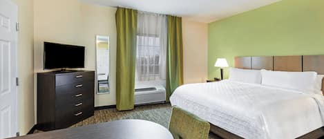 A hotel room with a bed, a TV, a desk with a chair, and a window with curtains.
