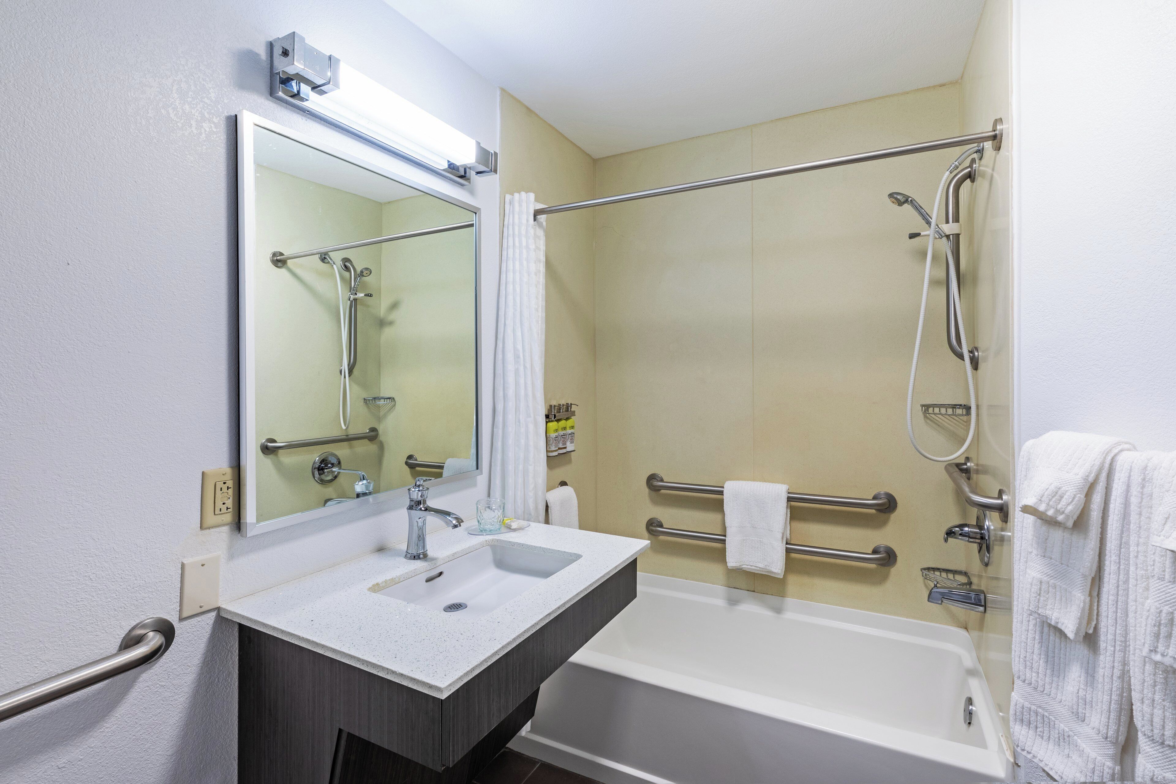 A bathroom with a white sink, a bathtub, a shower with a grab bar, a mirror, and a towel rack.