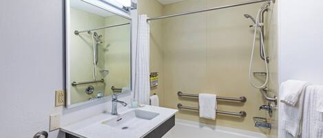 A bathroom with a white sink, a bathtub, a shower with a grab bar, a mirror, and a towel rack.