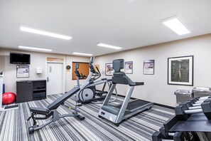 Ett gym med löpband, en crosstrainer och en motionscykel. Det finns en tv på väggen och en dörr med en skylt.