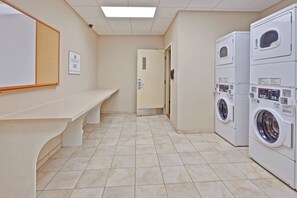 A laundry room with a bench, a sign indicating free washer and dryer, and a tiled floor. - Candlewood Suites Hattiesburg by IHG (Hattiesburg)