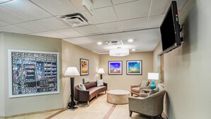 A lobby with a brown sofa, two armchairs, a round ottoman, and a large abstract art piece on the wall.