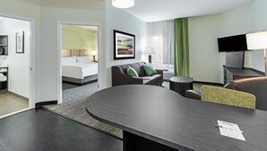 A hotel room with a bed, a sofa, a dining table, a TV, and a lamp.