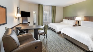 A hotel room with a bed, a desk, a chair, a TV, and a window with curtains.
