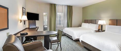 Una habitación de hotel con cama, escritorio, silla, televisión y ventana con cortinas.