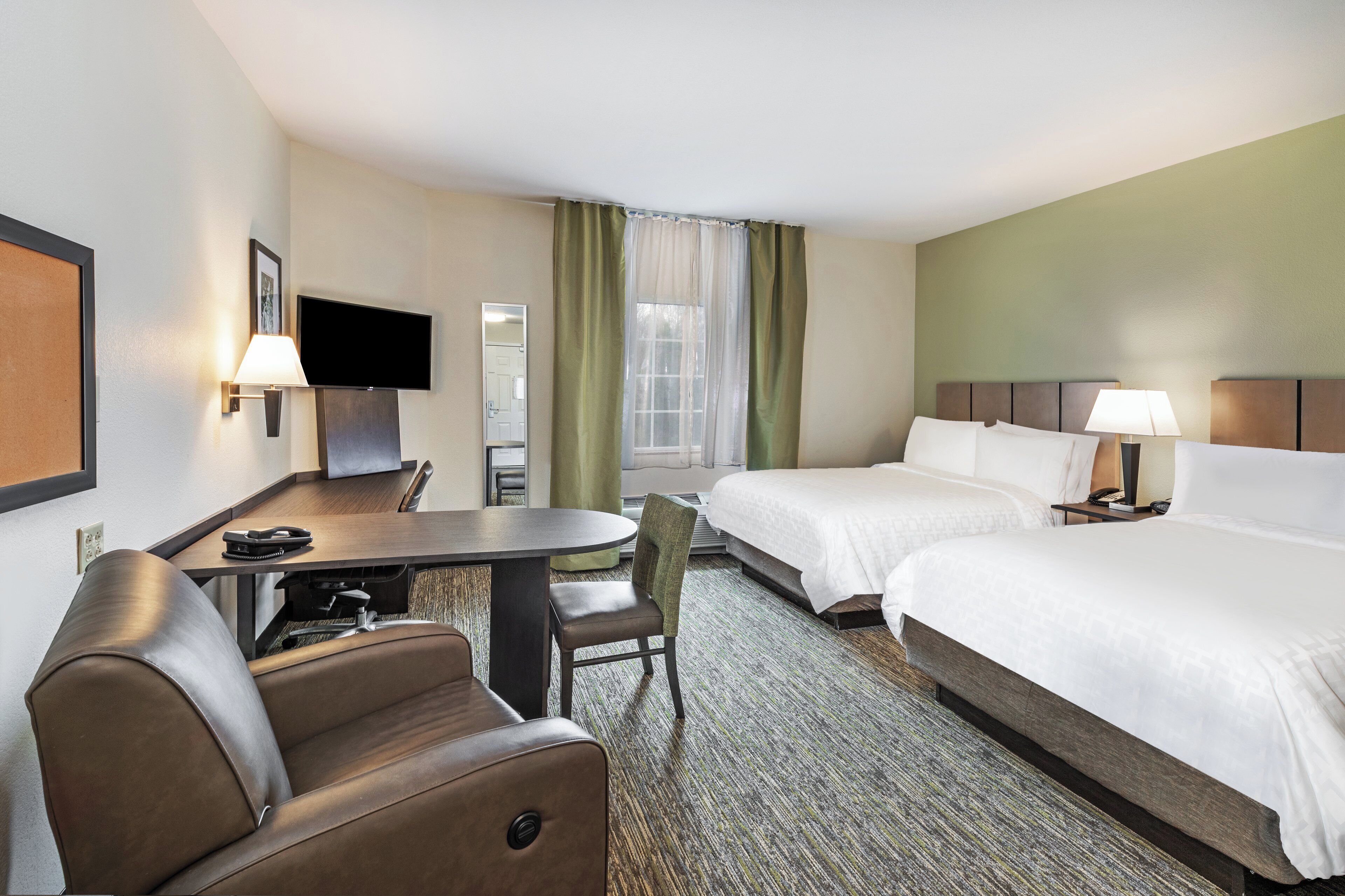A hotel room with a bed, a desk, a chair, a TV, and a window with curtains.