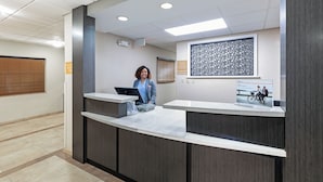 A reception desk with a computer, a framed artwork, and a window with blinds.