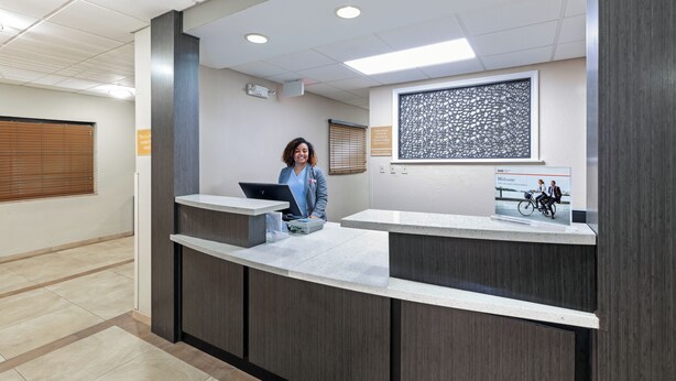A reception desk with a computer, a framed artwork, and a window with blinds.