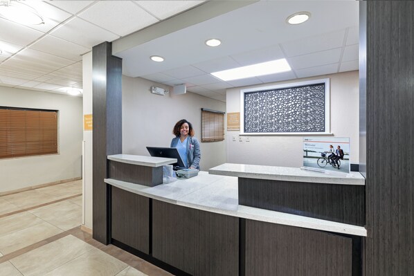 A reception desk with a computer, a framed artwork, and a window with blinds. - Candlewood Suites Hattiesburg by IHG (Hattiesburg)