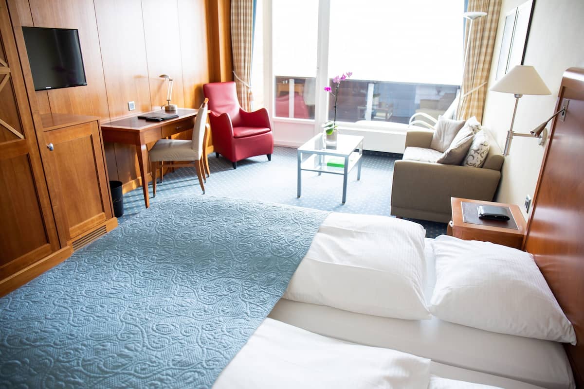 Ein Hotelzimmer mit einem Bett, einem Schreibtisch, einem roten Sessel, einer Couch, einem kleinen Tisch und einem Fernseher.