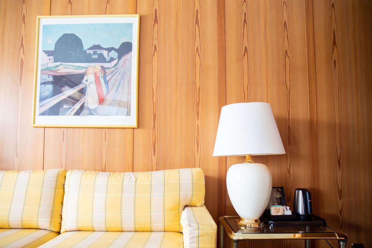 Ein Zimmer mit einer Wandpaneelaus Holz, einem gelb-gestreiften Sofa, einer weißen Lampe und einem gerahmten Bild.