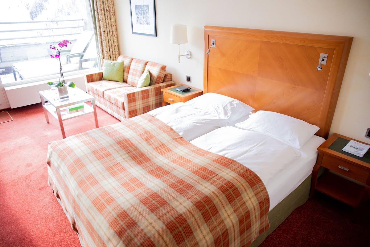 Ein Hotelzimmer mit Bett, einer Couch, einem kleinen Tisch und einem Fenster mit Vorhängen.