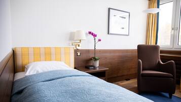 Habitación de hotel con cama, escritorio, silla, lámpara, planta y ventana con cortinas.