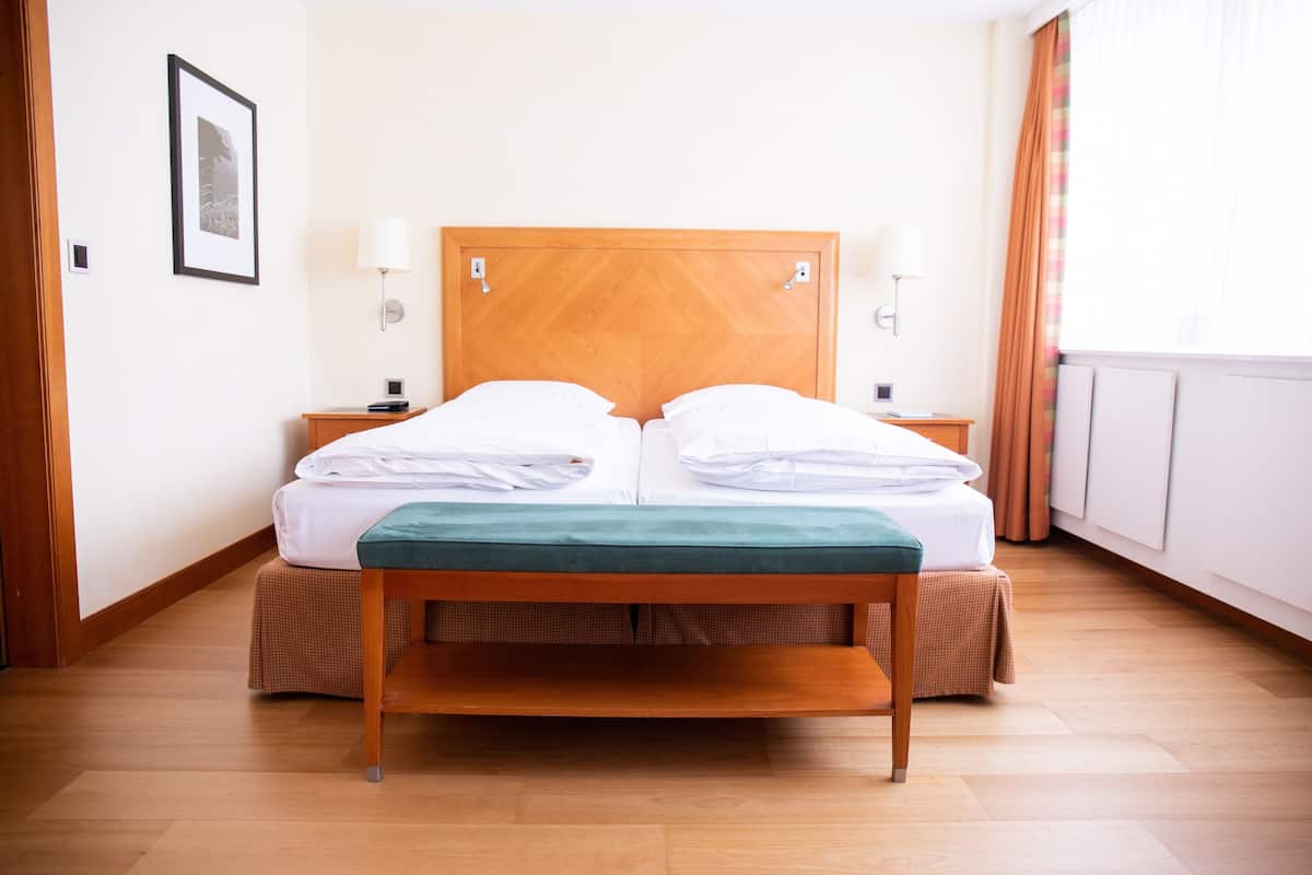 Ein Doppelbett mit Holz Kopfteil, zwei Nachttische mit Lampen, eine grüne Bank und ein gerahmtes Bild an der Wand.