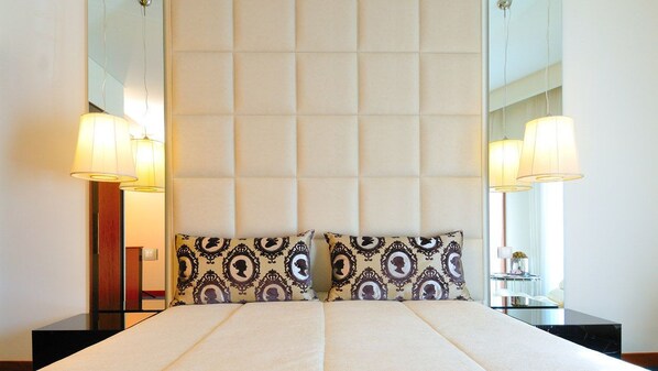 A hotel room with a large bed, two patterned pillows, a mirror above the bed, and two bedside lamps. - Hotel Moliceiro (Aveiro)
