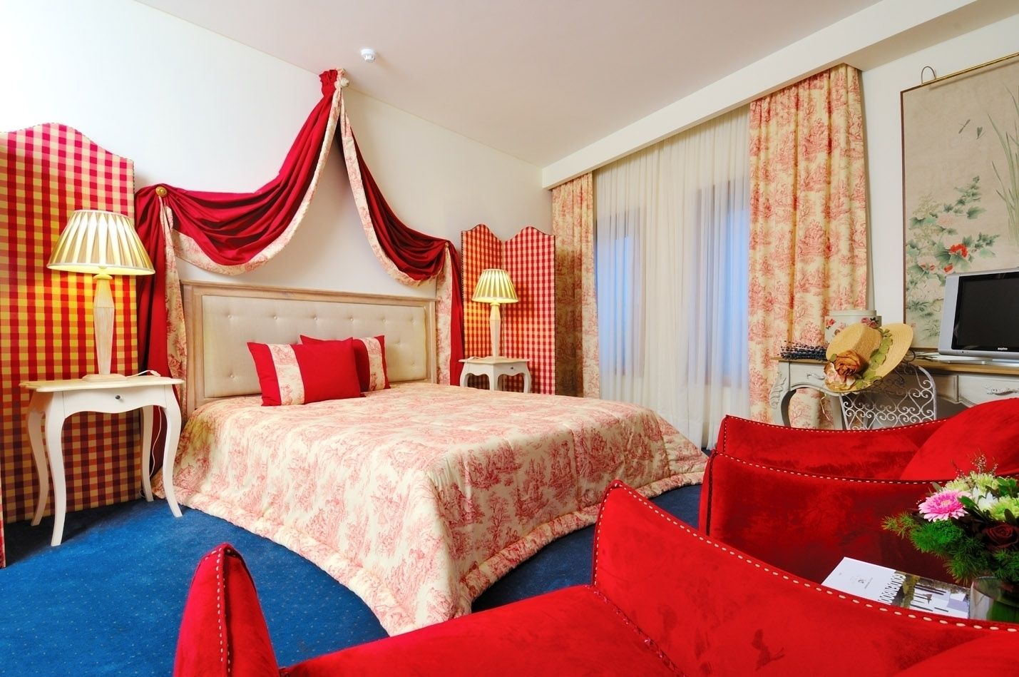 Ein Hotelzimmer mit einem großen Bett, roten und weißen Karottenvorhängen, einem Fernseher und einem Schreibtisch mit einer Lampe.