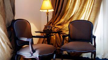 Deux fauteuils rembourrés, dotés d’une finition foncée et d’un tissu à motifs, sont placés autour d’une petite table sur laquelle se trouve une lampe.