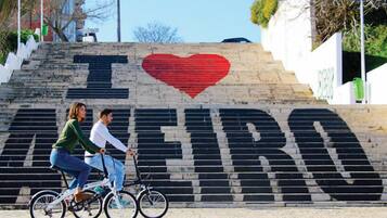 Ein Paar fährt mit einem Fahrrad eine Treppe hinauf, an deren Wand ein großes Wandbild mit der Aufschrift 'I LOVE FIRA' zu sehen ist.