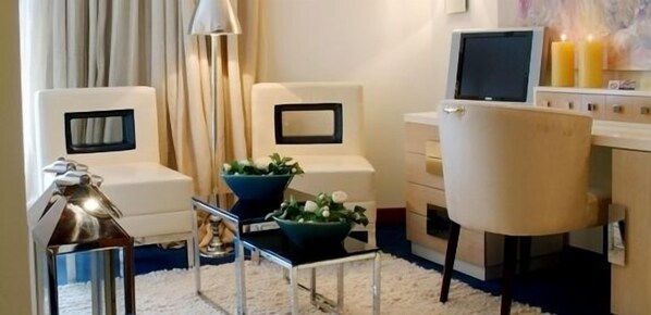 A modern living room with a sofa, a small table with a bowl of flowers, a lamp, and a TV. - Hotel Moliceiro (Aveiro)