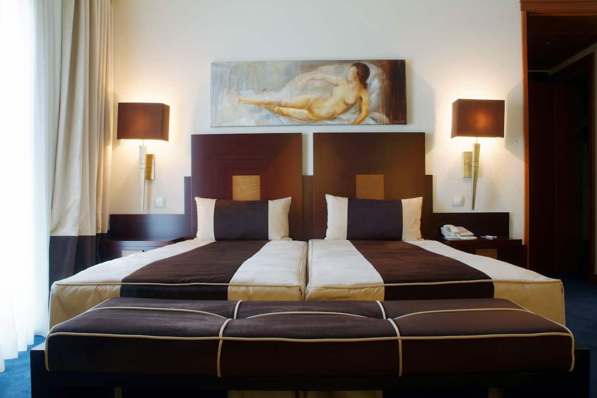 Una cama doble con cabecera, dos mesitas de noche, un cuadro sobre la cama y dos lámparas fijadas a la pared.
