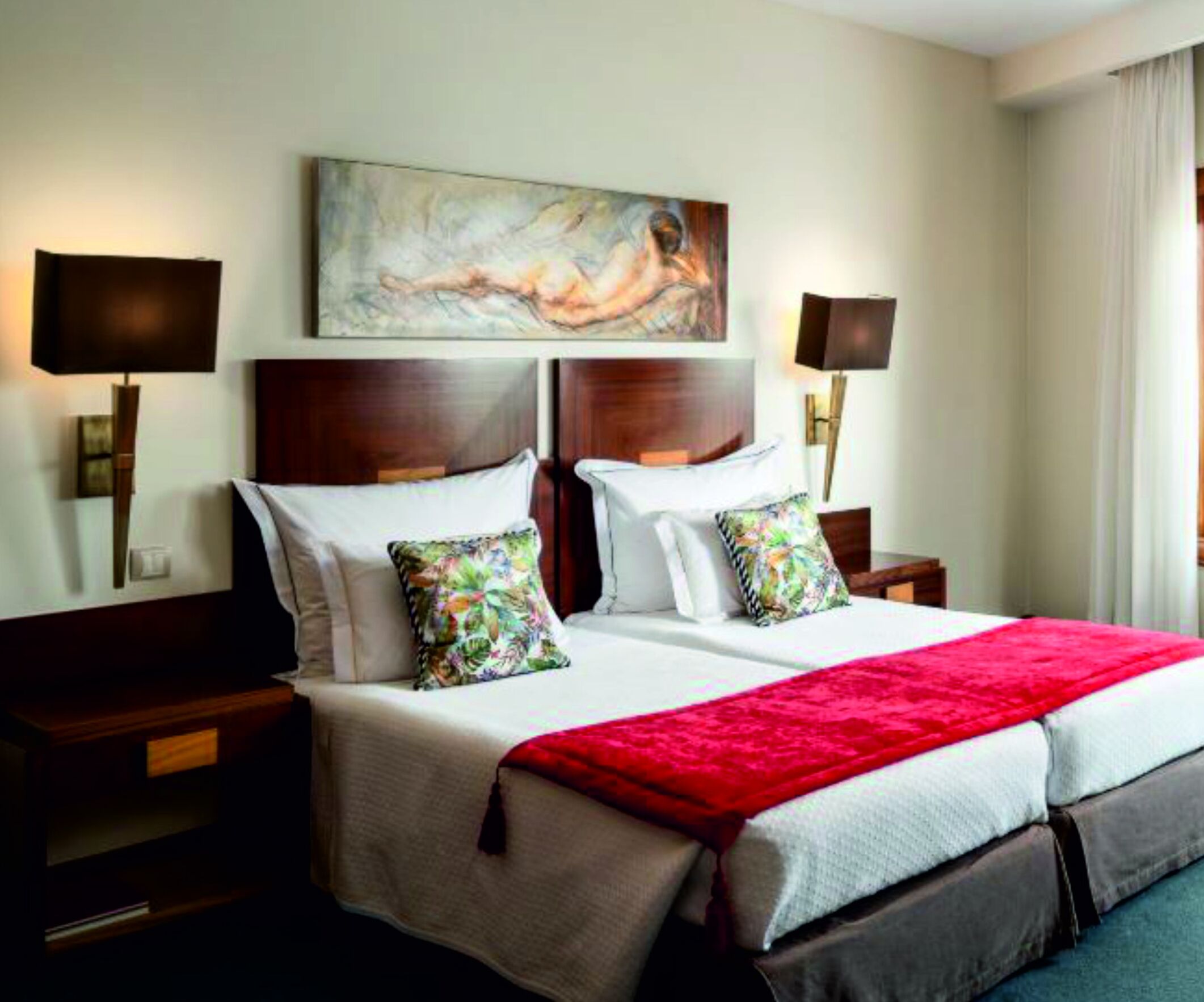 A hotel room with a large bed, two nightstands, a painting above the bed, and two wall lamps.