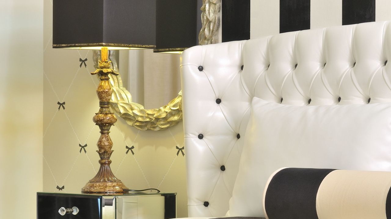 Un dormitorio lujoso con un cabecero capitonado, una lámpara decorativa y una mesita de noche con espejo.