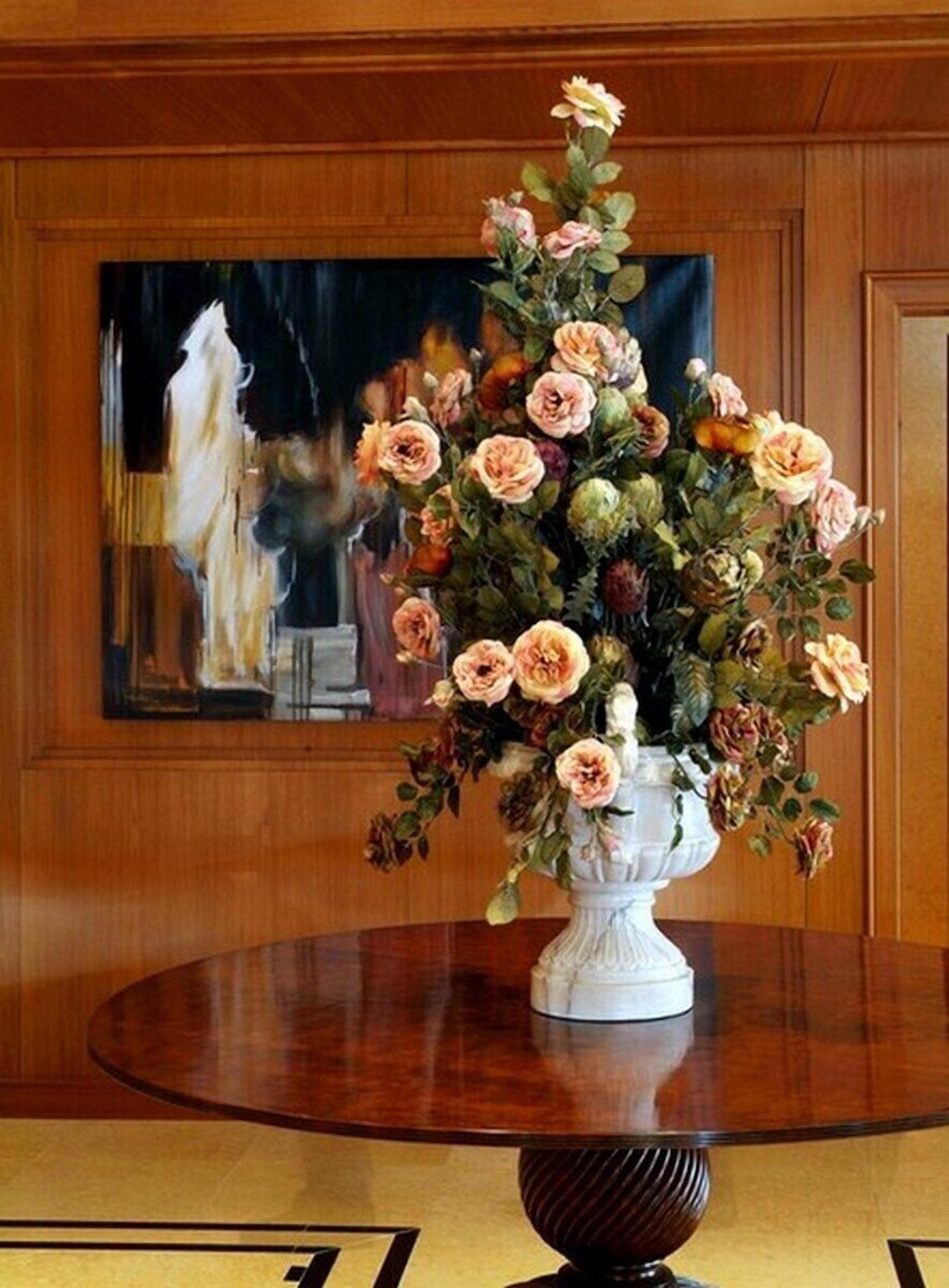 A round wooden table with a white vase containing a bouquet of flowers.