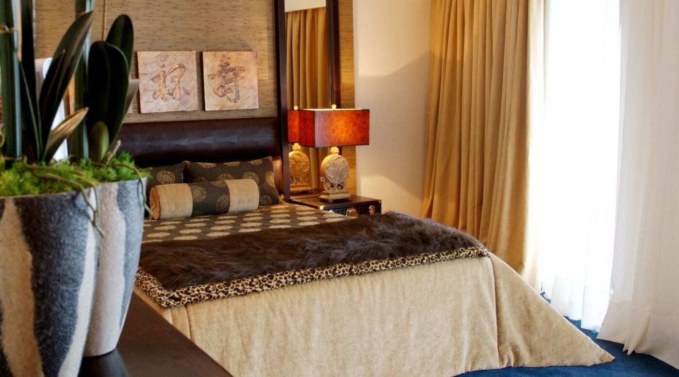Quarto de hotel com uma cama grande, mesa de cabeceira com duas luminárias, planta em vaso e obras de arte na parede.