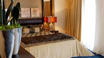 Quarto de hotel com uma cama grande, mesa de cabeceira com duas luminárias, planta em vaso e obras de arte na parede.