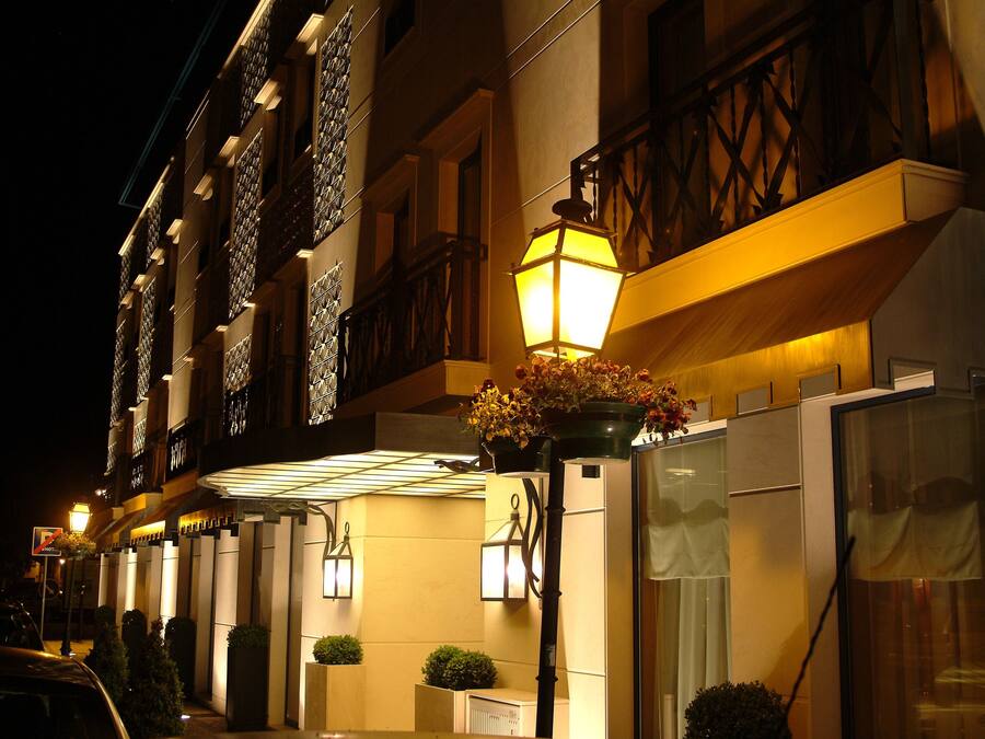 La façade d’un hôtel de nuit, avec des fenêtres illuminées, un balcon doté d’une balustrade et un lampadaire orné de fleurs.